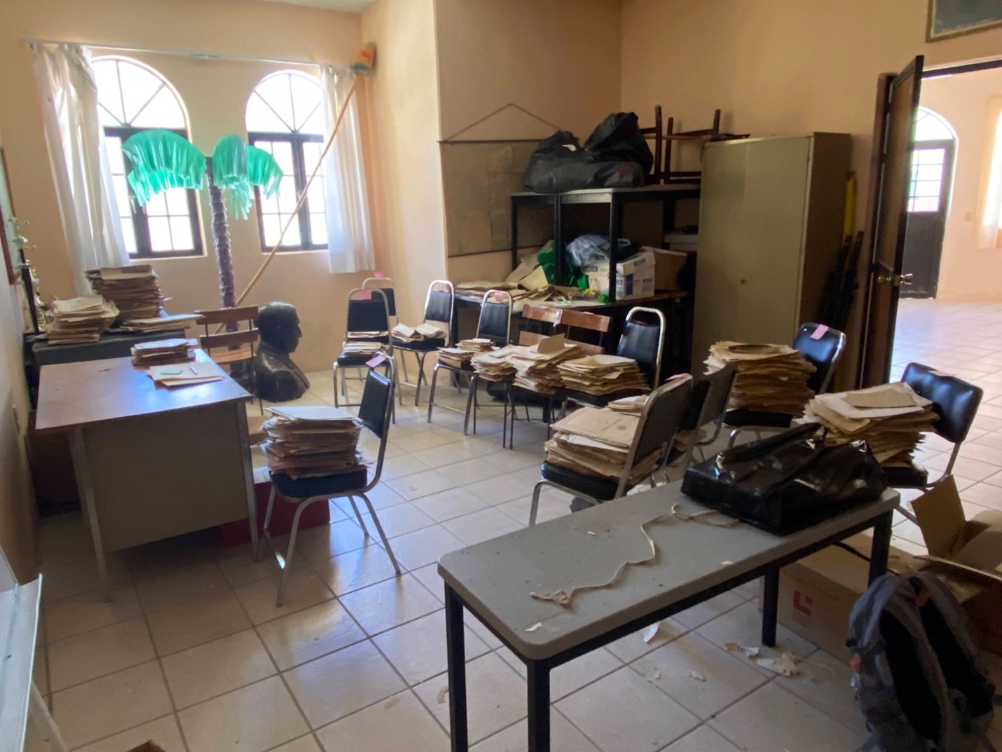 Messy room with documents on tables and chairs.